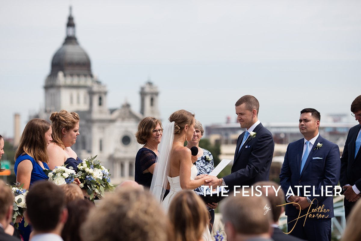 A bride and groom stand at the "alter" with their wedding party on a rooftop overlooking the Minneapolis skyline.